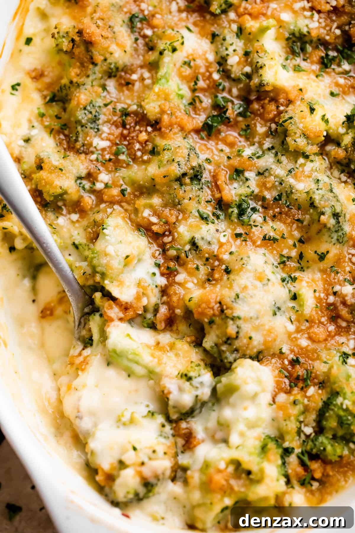overhead shot of an oval baking dish with Cheesy Broccoli Casserole and a spoon mixing through it.