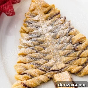 A baked puff pastry Christmas tree, dusted with powdered sugar, on an oval platter. Christmas greenery, a red bow, and a small bowl of chocolate dipping sauce surround the platter.