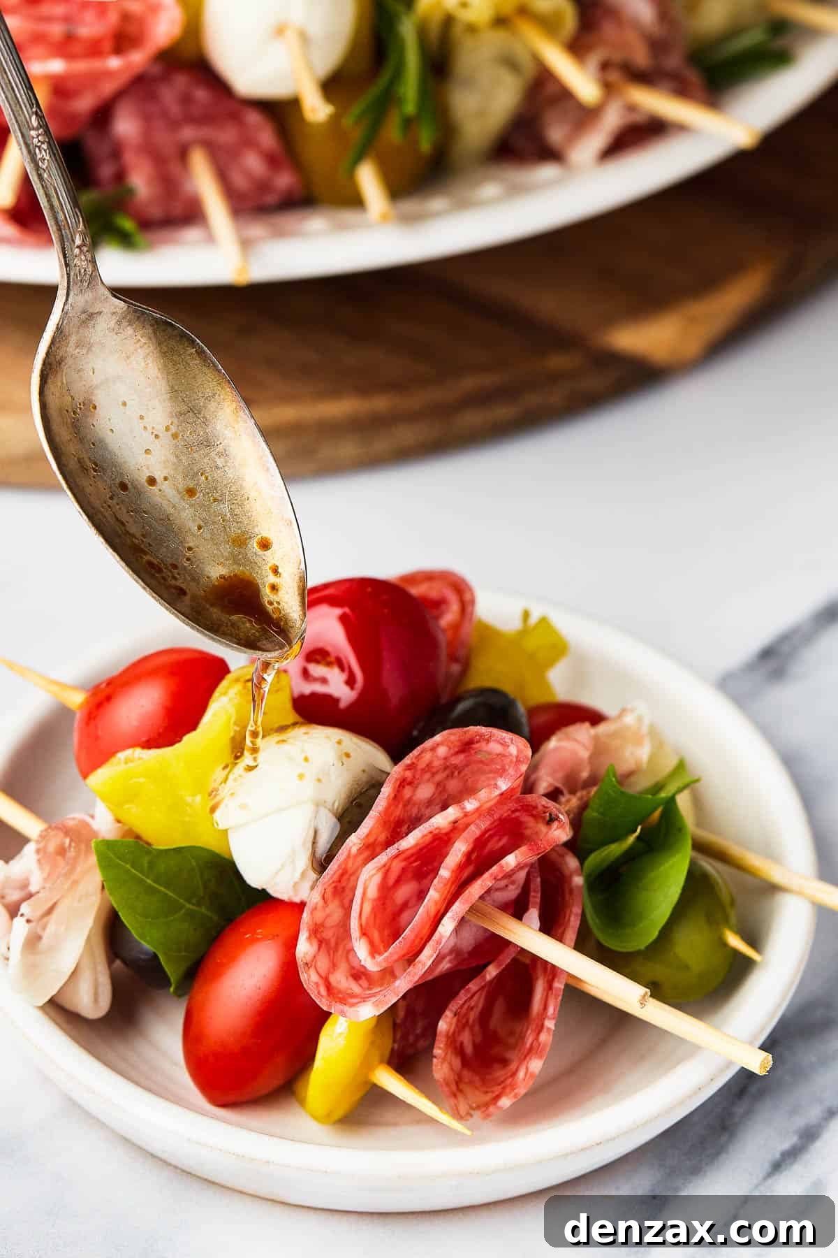 A spoon drizzling balsamic vinegar over a serving of antipasto.