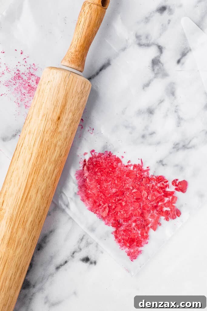 Hard candies crushed on a marble work surface. A rolling pin is on the surface next to the candies.