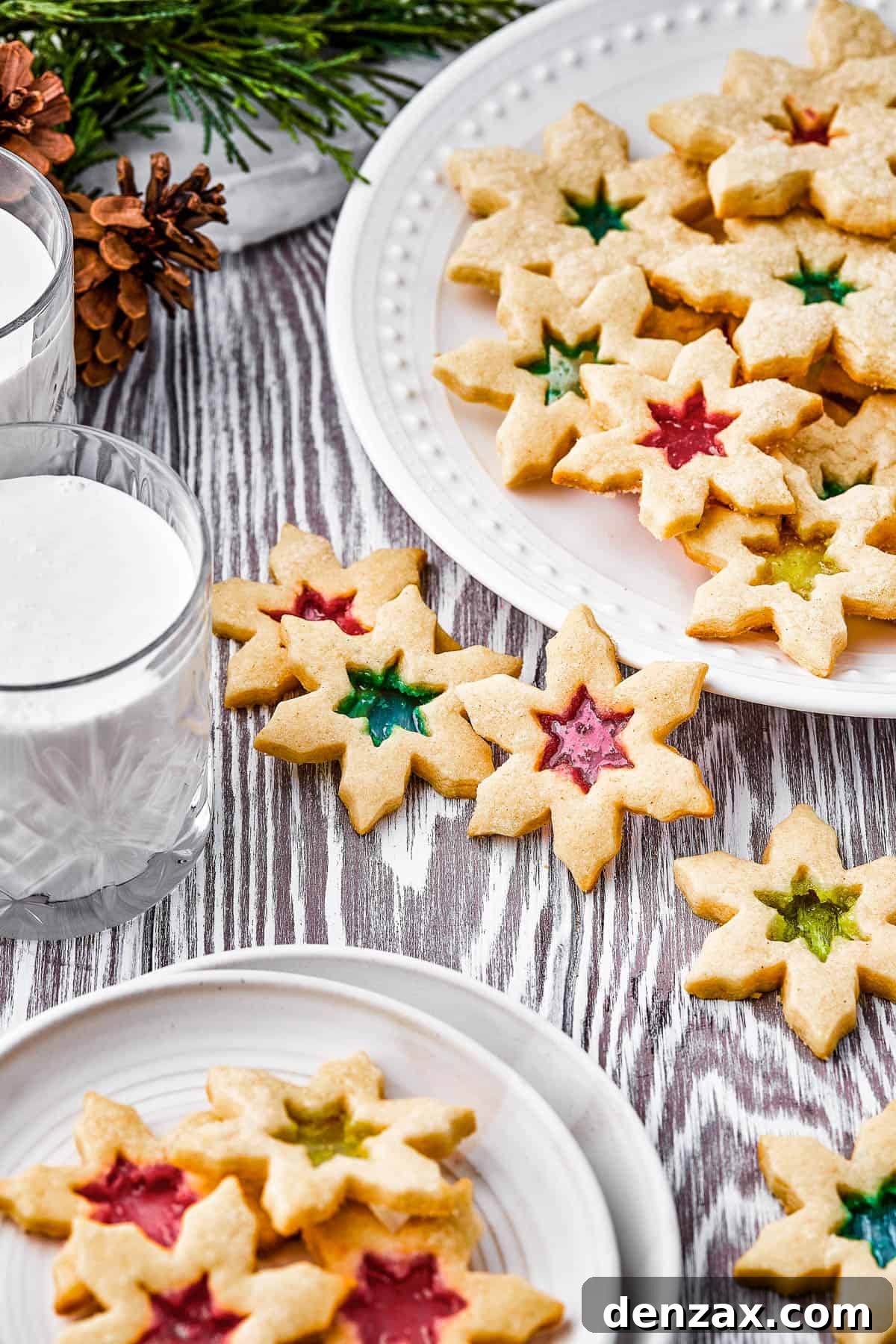 Two plates of stained glass cookies, with extra cookies arranged artistically on the table, along with a glass of milk.
