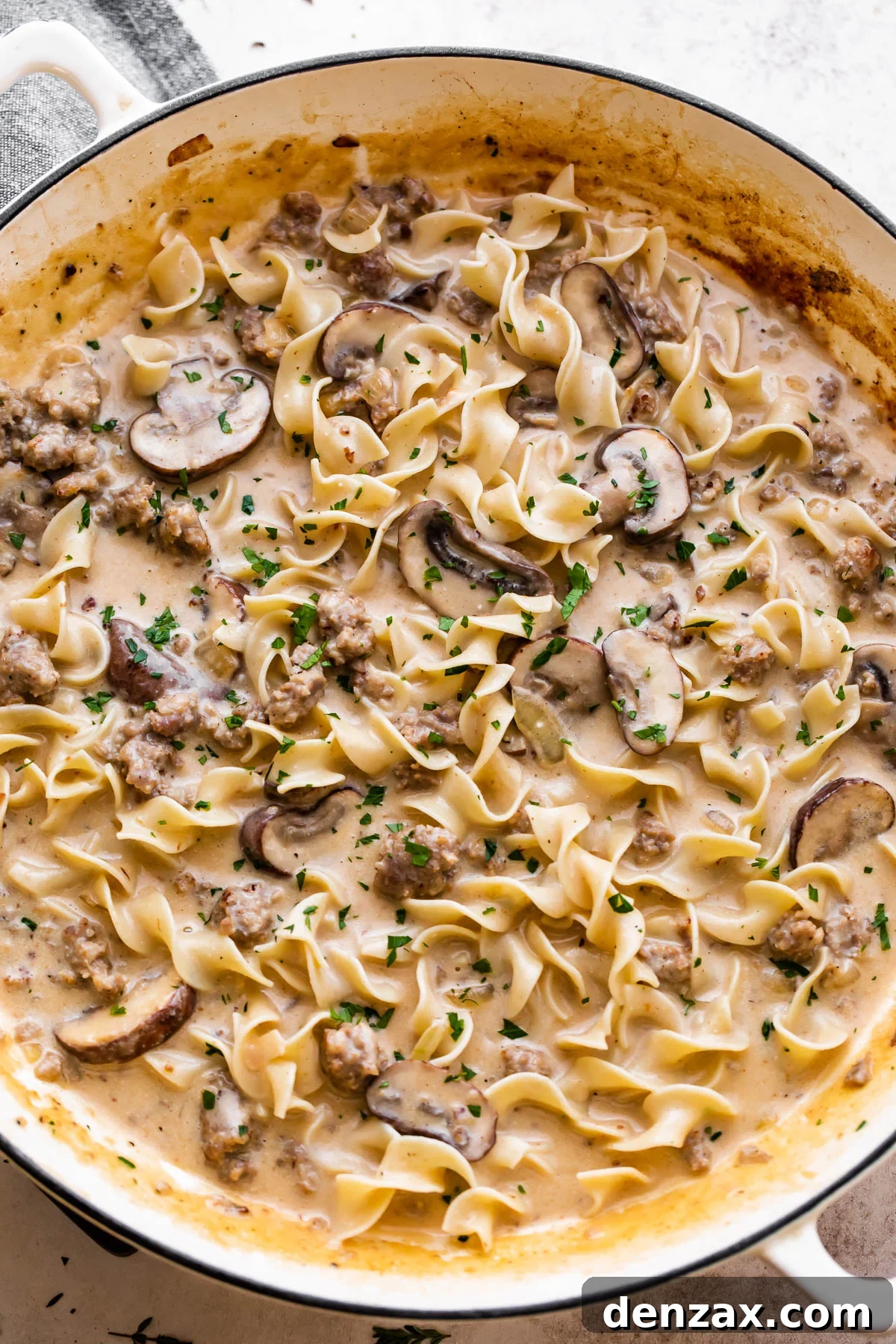 overhead shot of a white braiser filled with cream sauce, noodles, mushrooms, and beef.