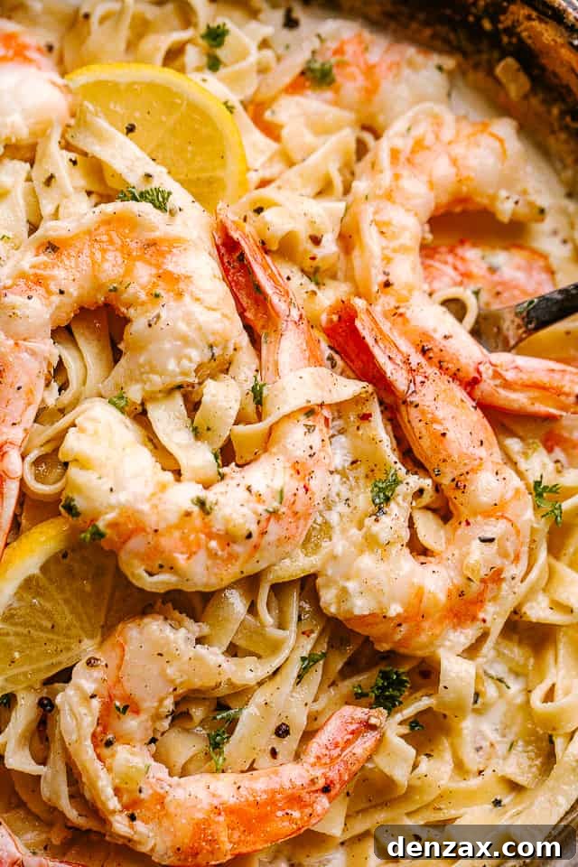 Close up of Creamy Shrimp Alfredo Pasta in a pan garnished with lemon wedges.