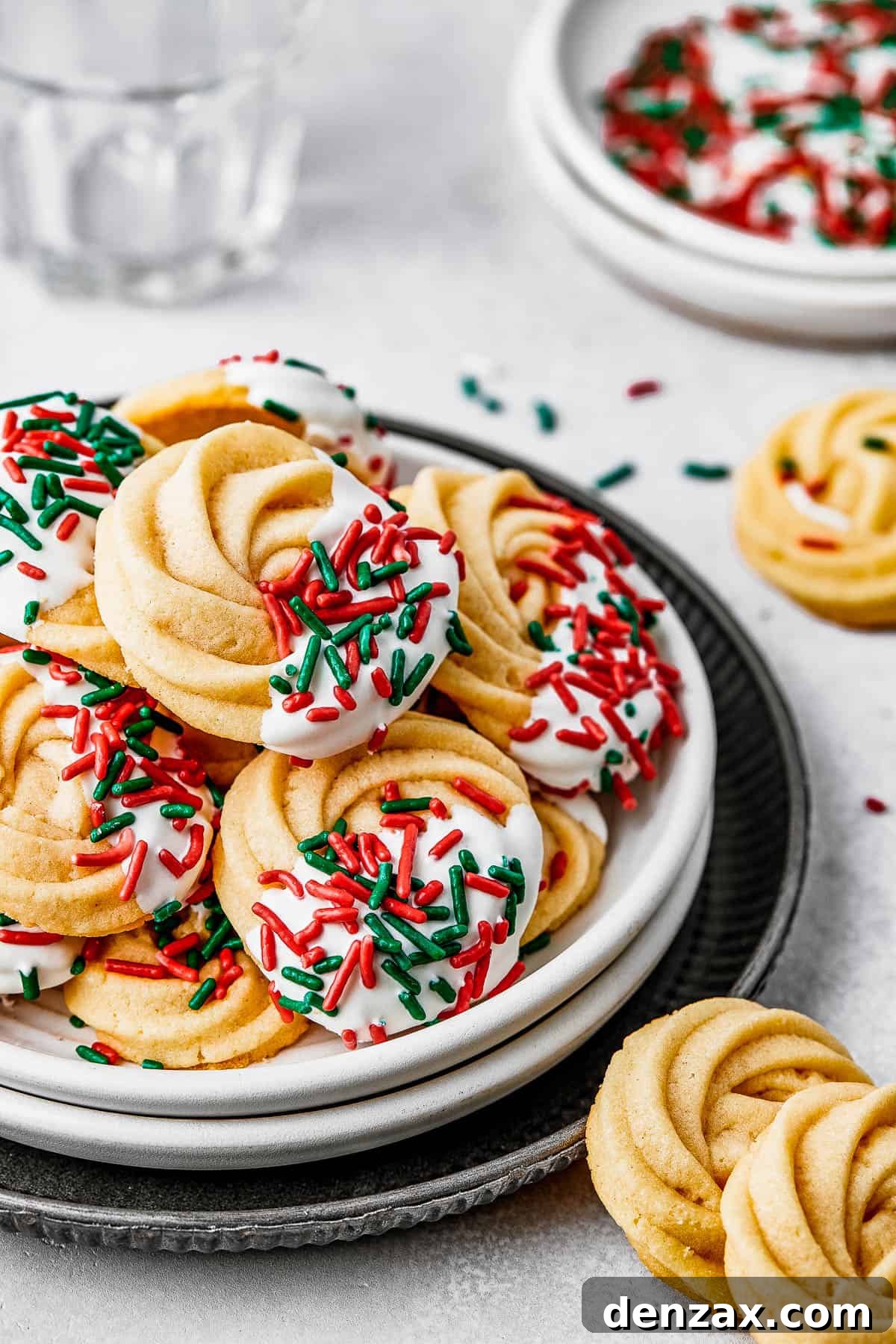 A small dessert plate stacked on top of several other plates, and piled with iced butter cookies.