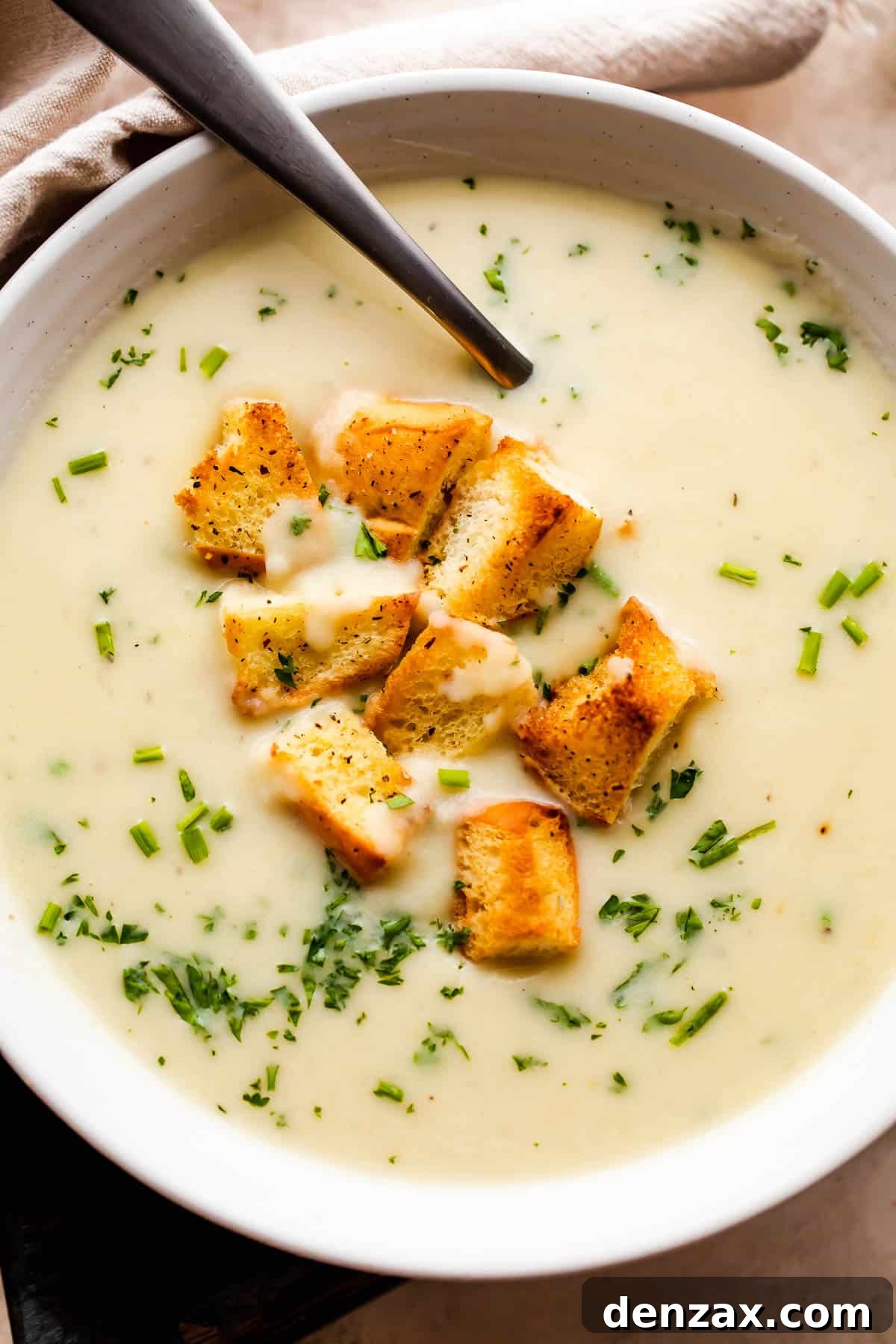 overhead close up shot of leek and potato soup served in a white bowl and garnished with croutons and chopped chives.