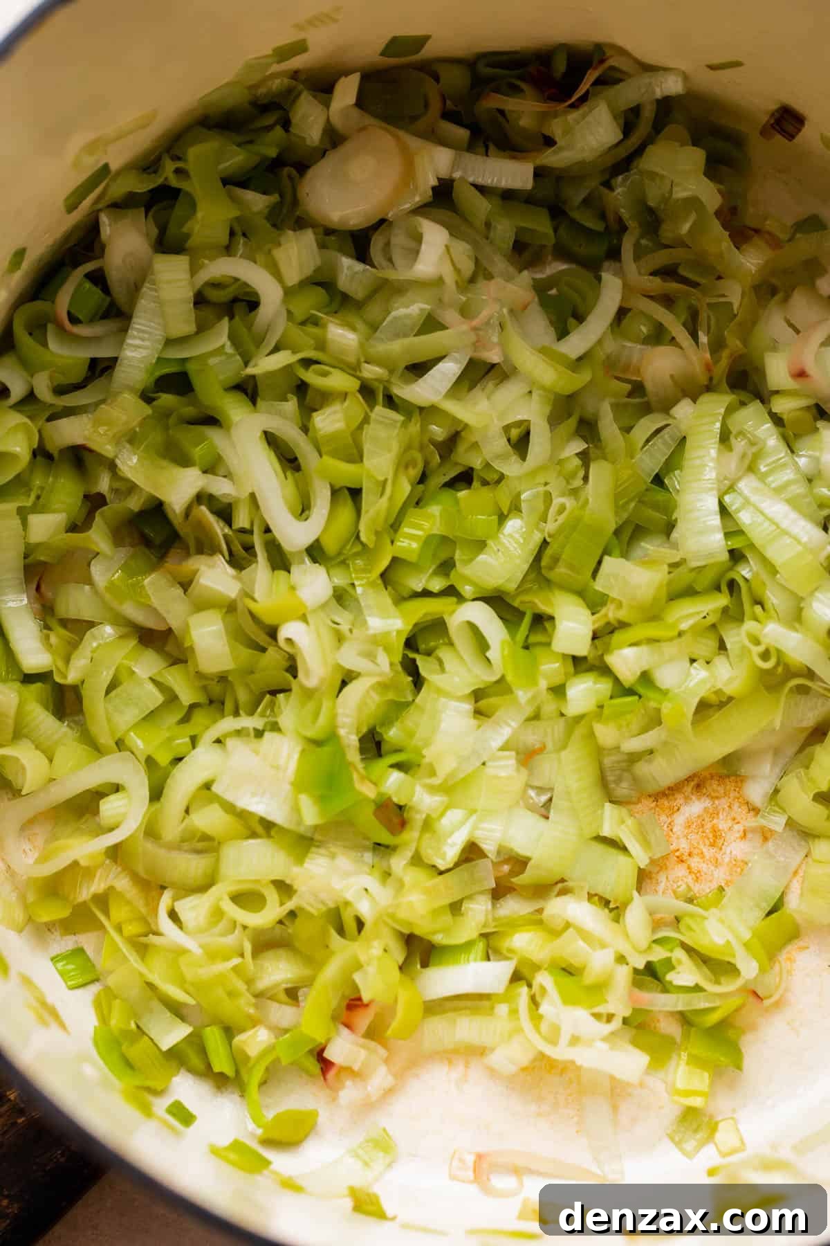 frying sliced leeks in a white dutch oven.