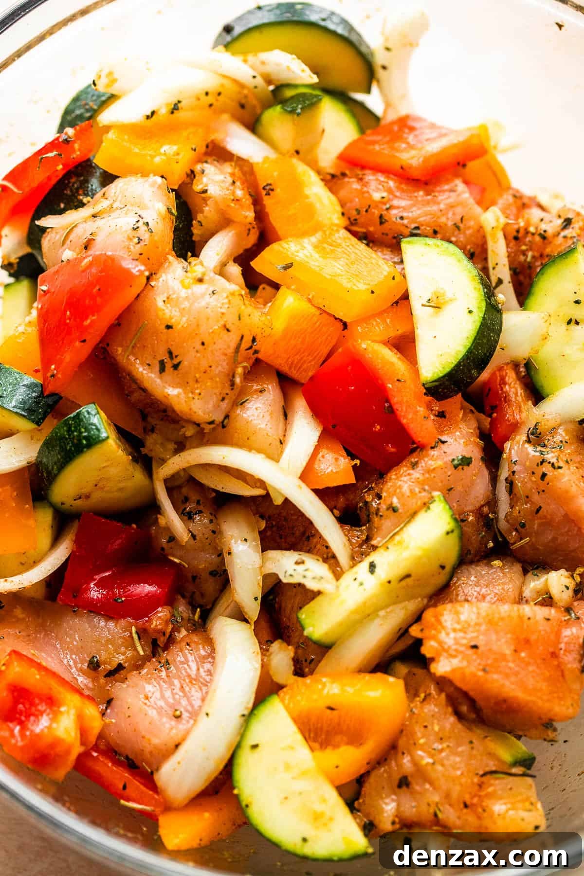 chicken pieces, sliced zucchini, peppers, and onions in a glass mixing bowl.