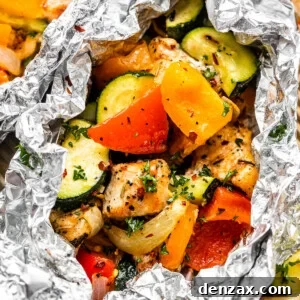 overhead shot of diced chicken, sliced zucchini, and sliced peppers all layered in an aluminum foil packet.