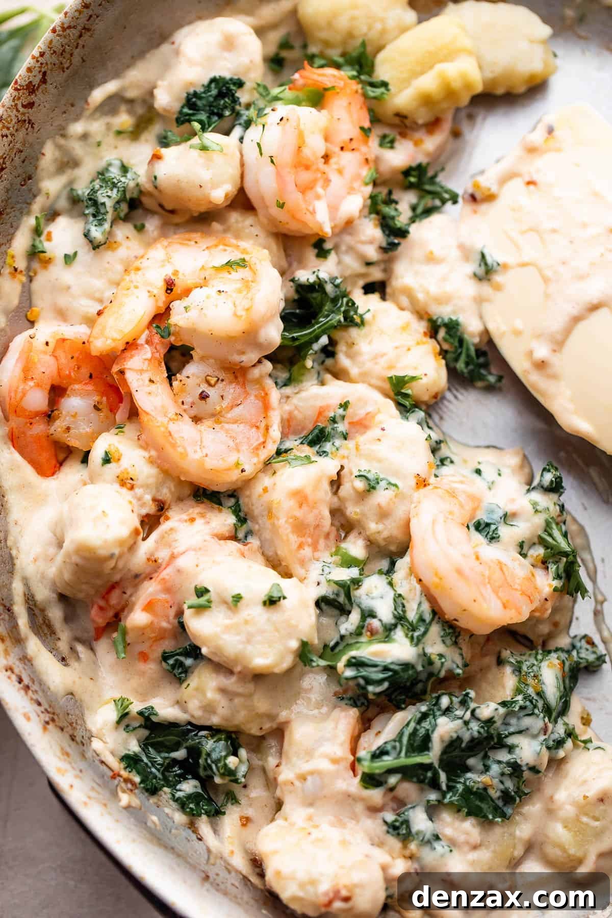 up close shot of a steel skillet filled with cream sauce, gnocchi, shrimp, and greens.