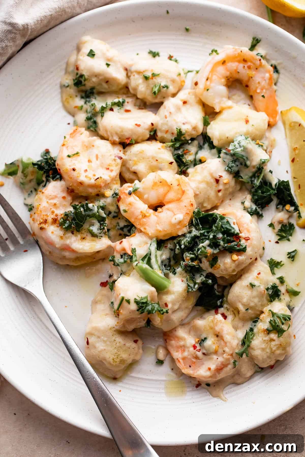 overhead shot of creamy gnocchi with shrimp served on a white plate with a fork placed to the left side on the plate.