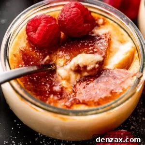side shot of creme brulee in a glass jar, topped with two raspberries, and a spoon inside the jar.