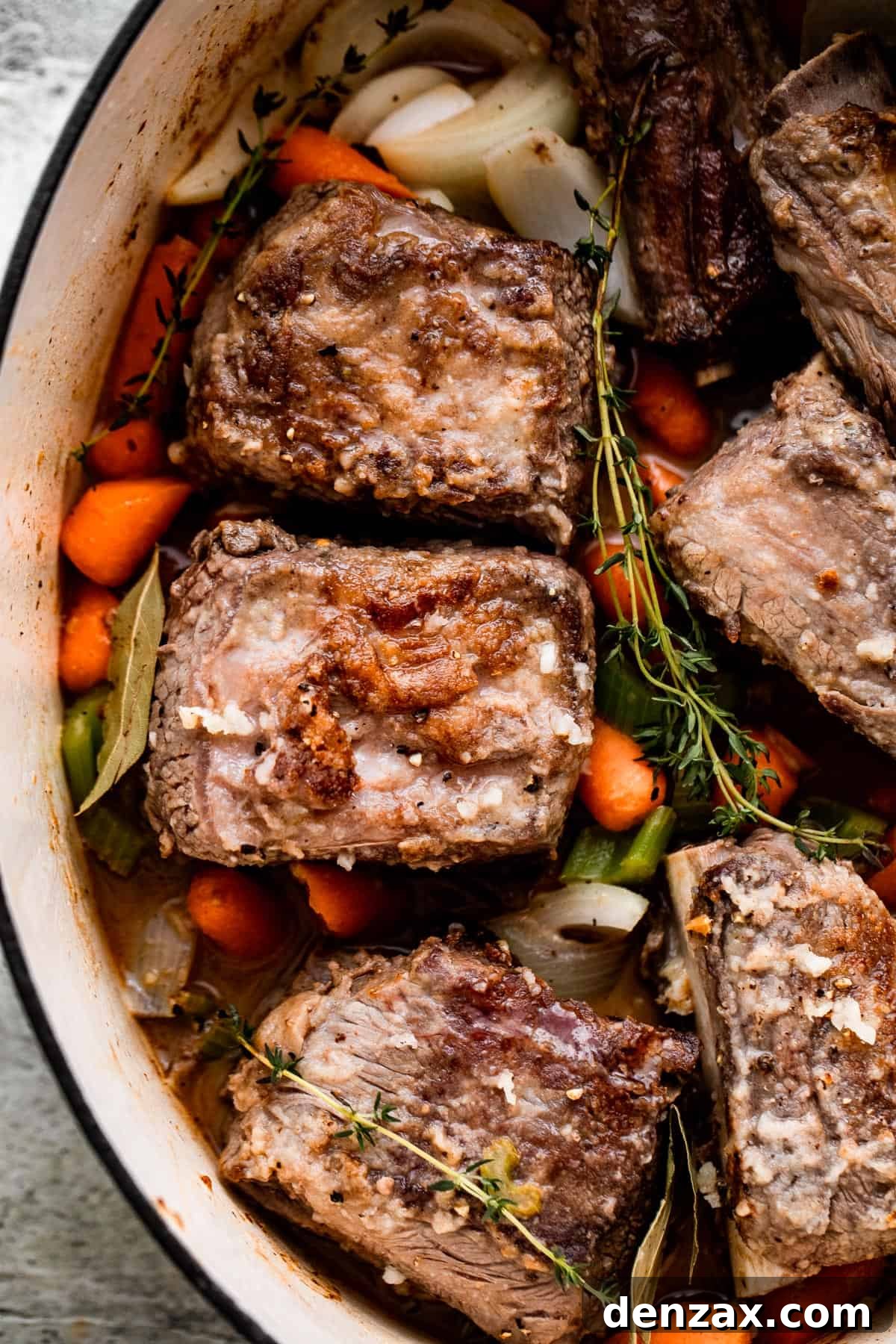 carrots, onions, thyme sprigs, and beef short ribs arranged inside the slow cooker insert.