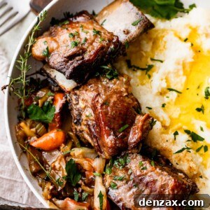 overhead shot of a dinner plate with three short ribs arranged around mashed potatoes, with veggies and onions set on the other side of the short ribs.