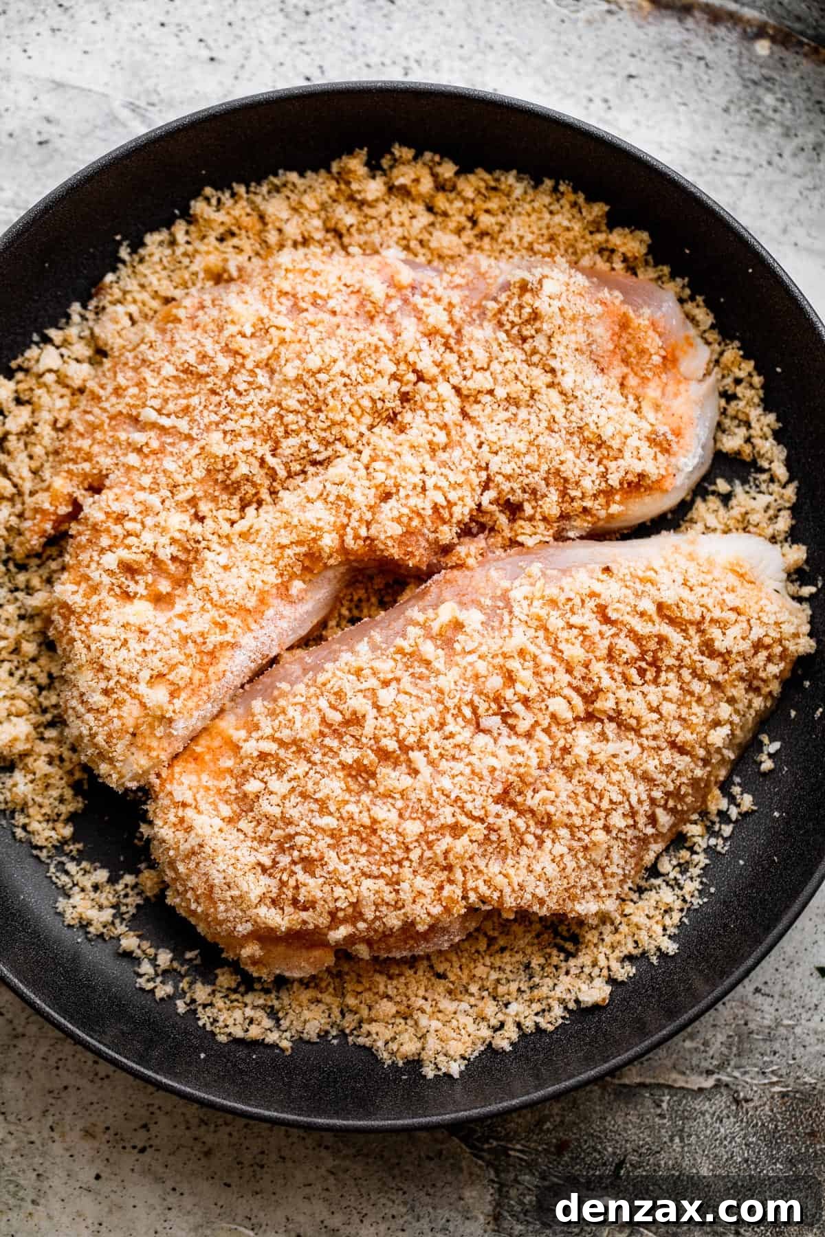 Crispy Chicken Schnitzel Recipe with Lemon and Herb Breadcrumbs 4 overhead shot of breaded chicken set on a black plate.