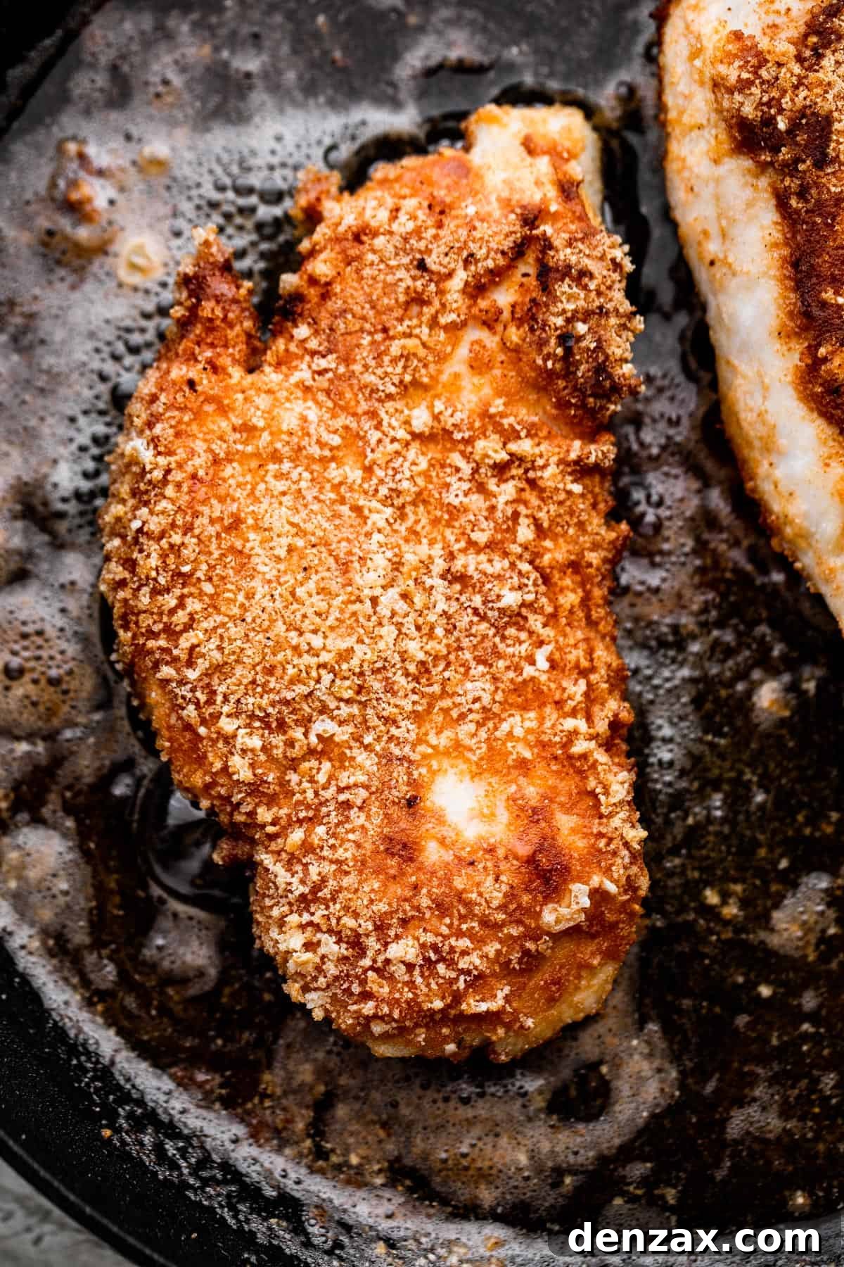 Crispy Chicken Schnitzel Recipe with Lemon and Herb Breadcrumbs 5 overhead shot of breaded chicken frying in a black skillet.