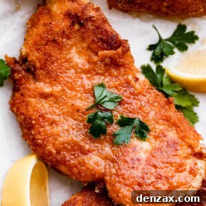 Crispy Chicken Schnitzel Recipe with Lemon and Herb Breadcrumbs 8 up close shot of chicken schnitzel garnished with parsley and lemon wedges placed around the chicken.