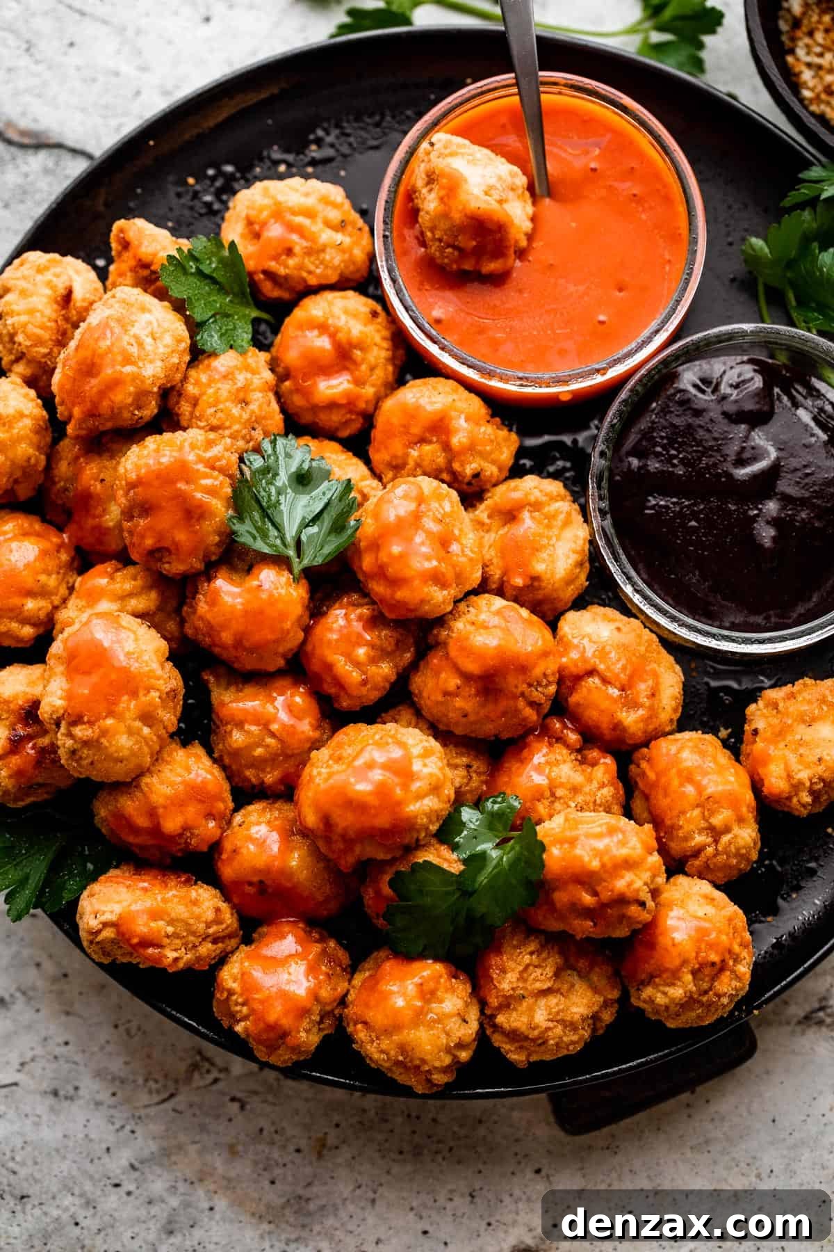 overhead shot of popcorn chicken arranged on a black plate with bowls of buffalo sauce and barbecue sauce placed right next to it.