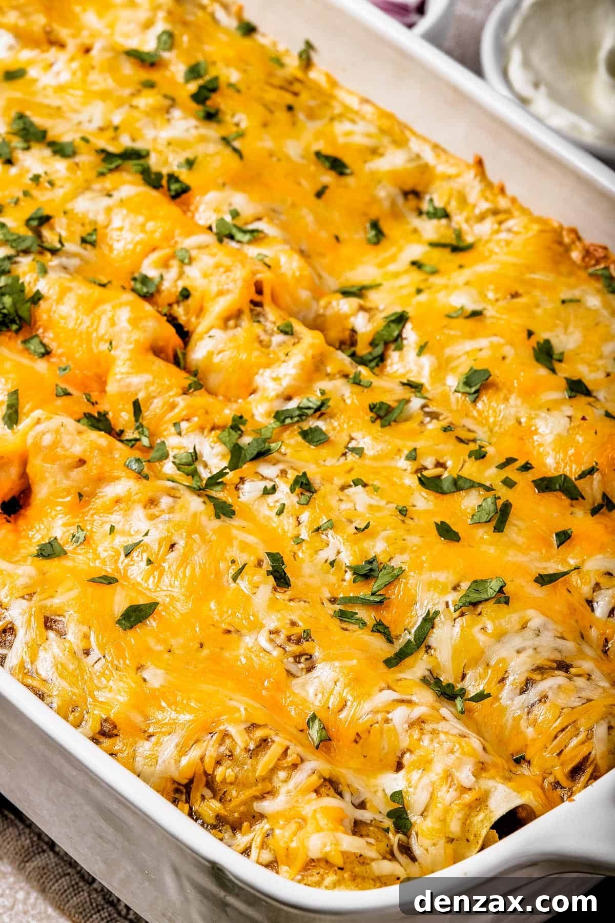 Close-up of a baking dish of cheesy enchiladas, sprinkled with fresh herbs.
