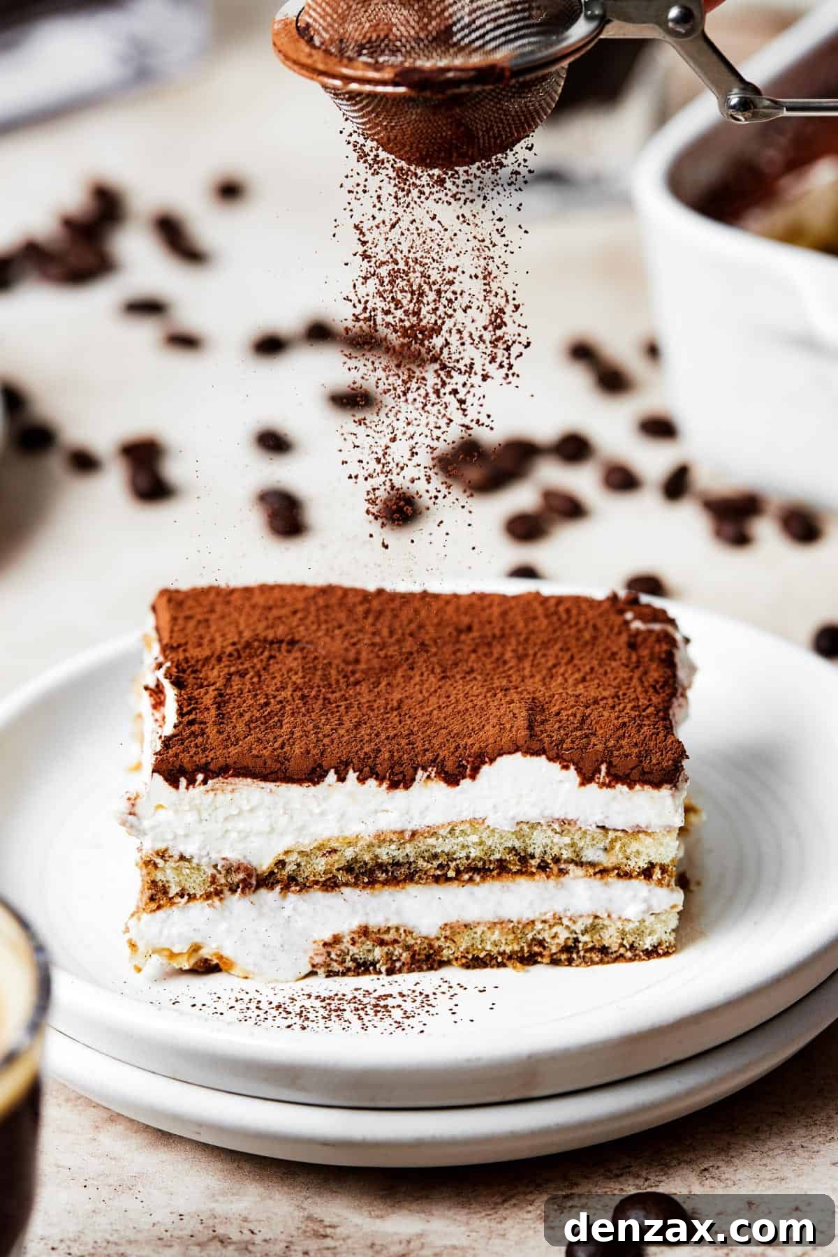 A square of tiramisu on a dessert plate, with the layers visible from the side.