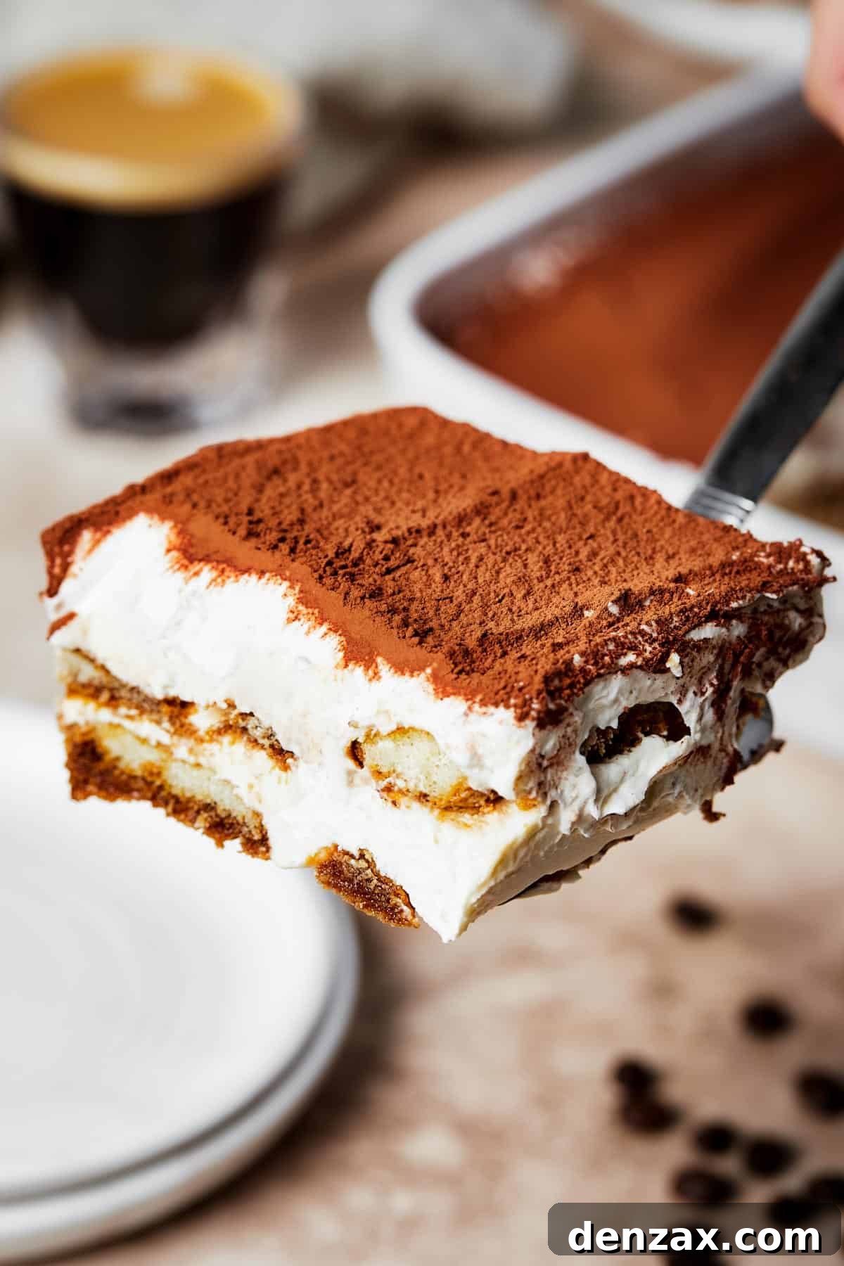 A square of tiramisu on a serving utensil being placed on a dessert plate.