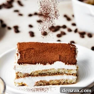 A square of tiramisu on a dessert plate, with the layers visible from the side.