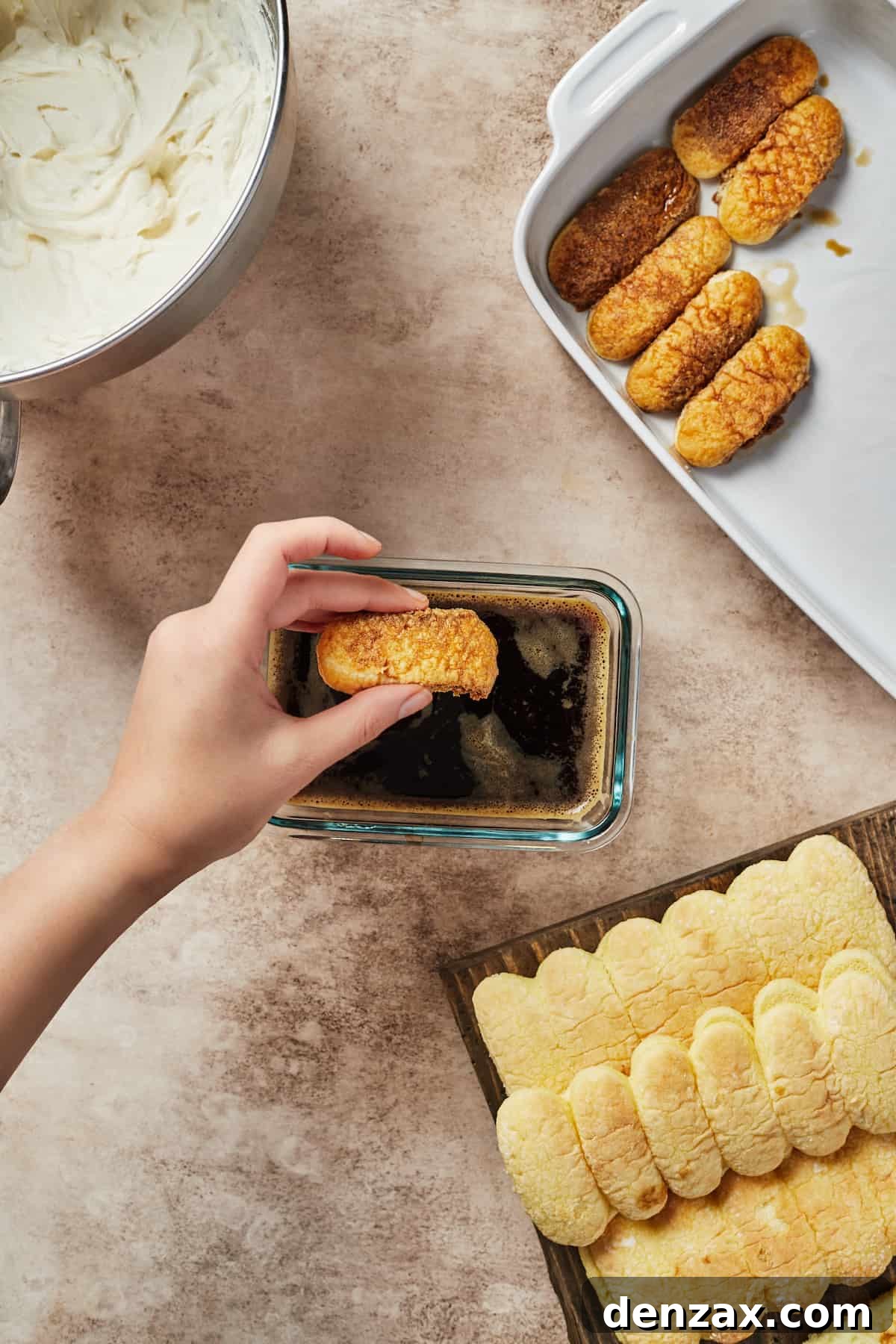 A woman's hand dipping savoiardi cookies into a rectangular glass dish of espresso.