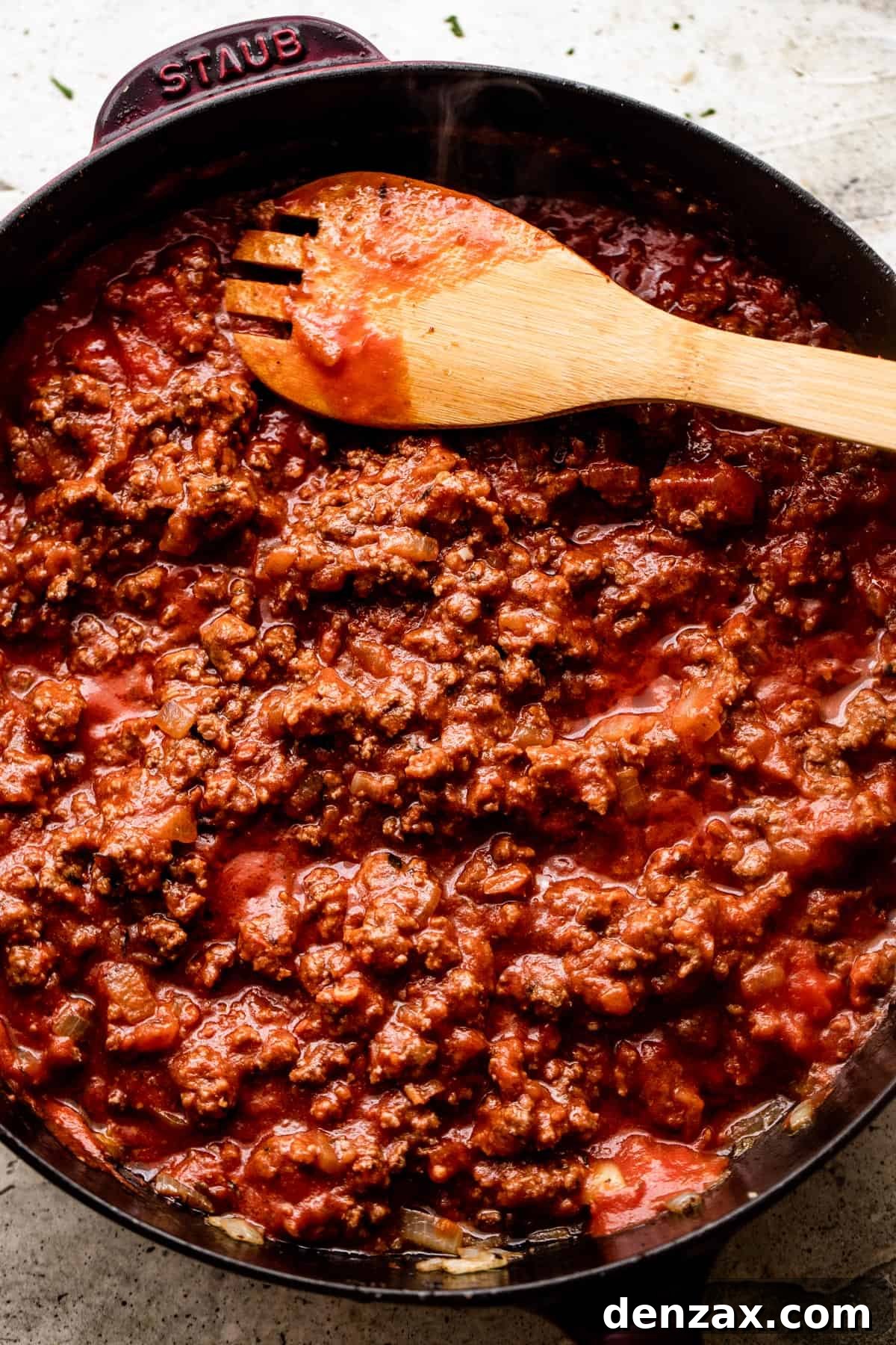 wooden spoon stirring through ground beef that's cooking in a black skillet.