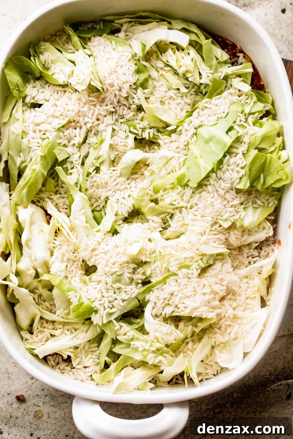 overhead shot of chopped cabbage and dry rice inside a white baking dish