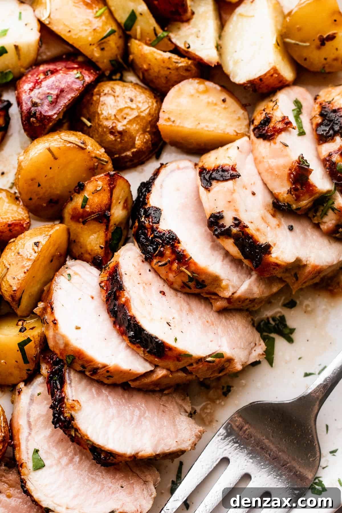 close up shot of sliced roast pork tenderloin served with colored baby potatoes