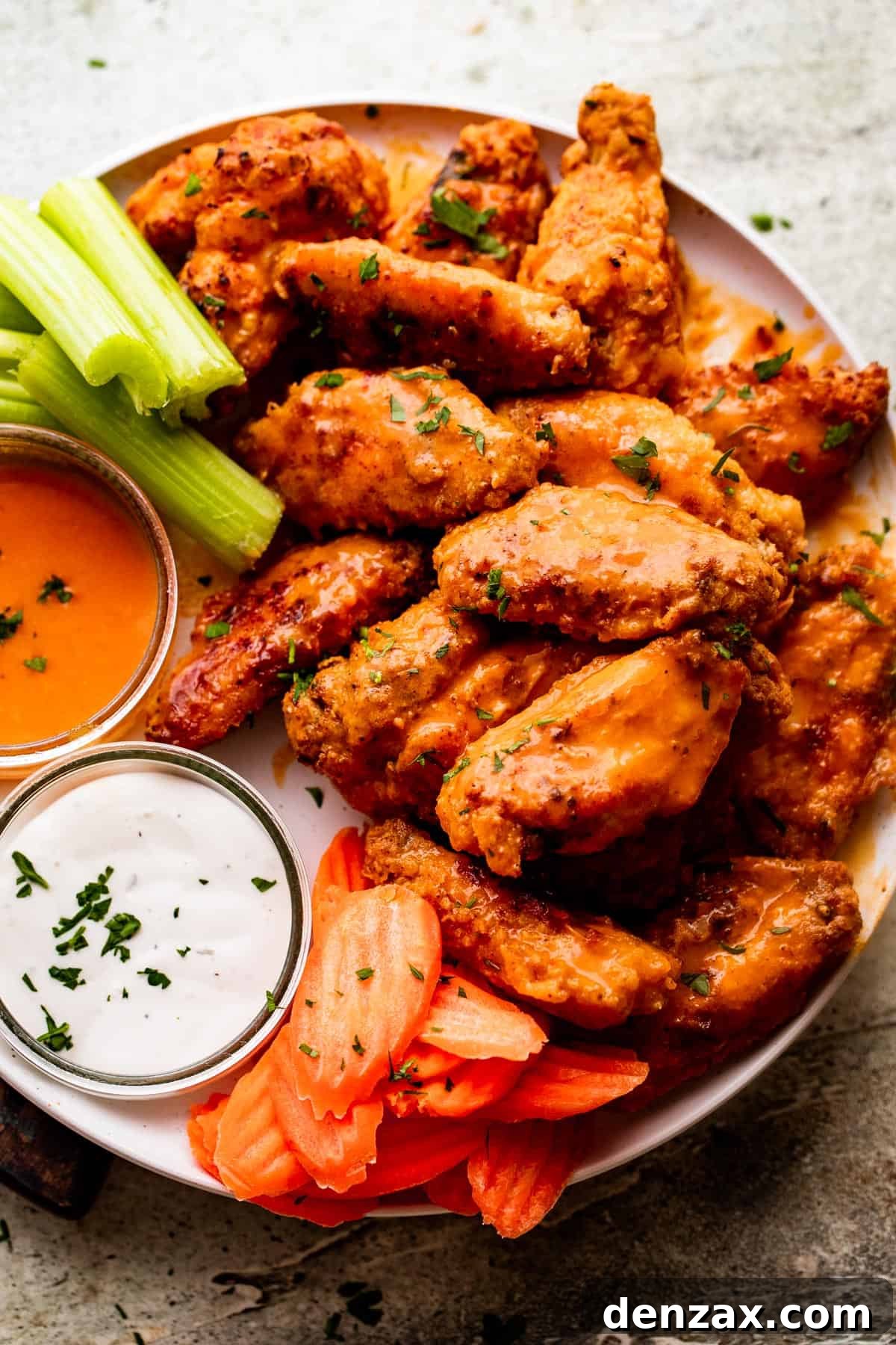overhead shot of Mango Habanero Hot Wings arranged on a white serving plate with celery sticks and carrots set alongside the wings. Two Jars of hot sauce and ranch dipping sauce are also set on the plate.
