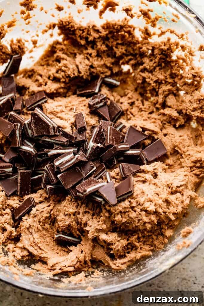 overhead shot of cookie dough in a mixing bowl with chopped chocolate mints in the center of the dough.
