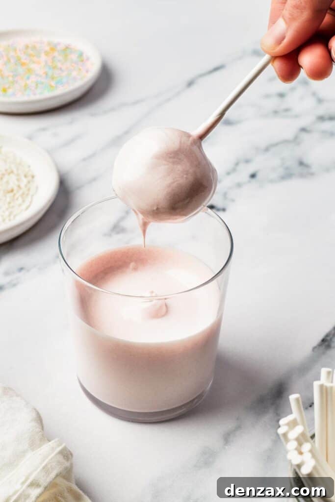 A ball of cake being dipped into a glass of melted candy coating.
