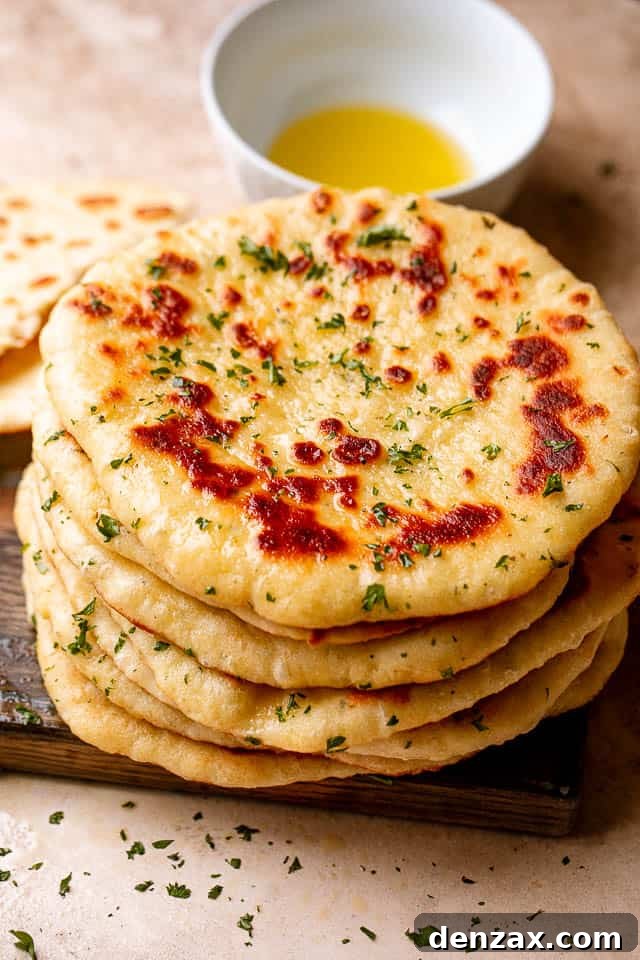 Top view of a stack of homemade flatbread on a wooden board next to a bowl of olive oil.