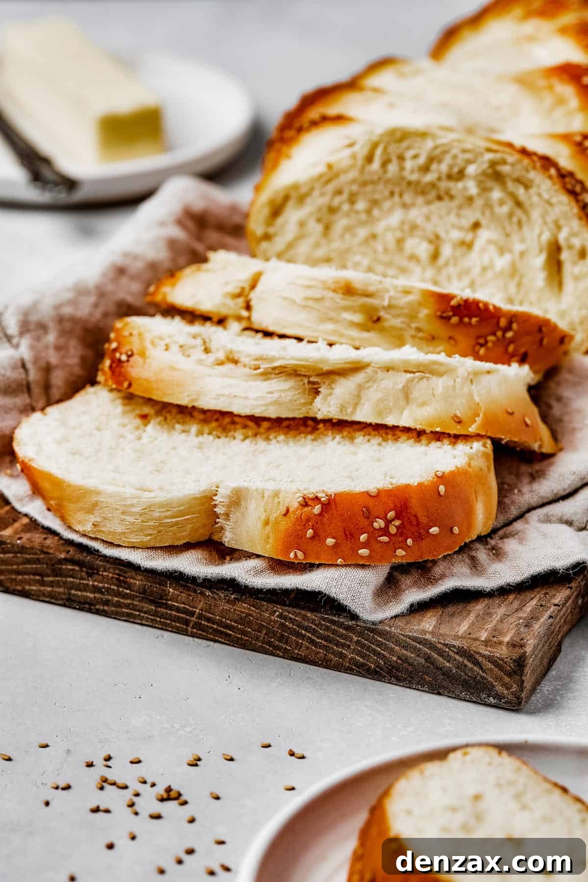 Classic Homemade Challah Recipe: Soft, Fluffy Braided Bread 4 A wooden cutting board lined with a tea towel. Sliced braided bread is arranged on top.