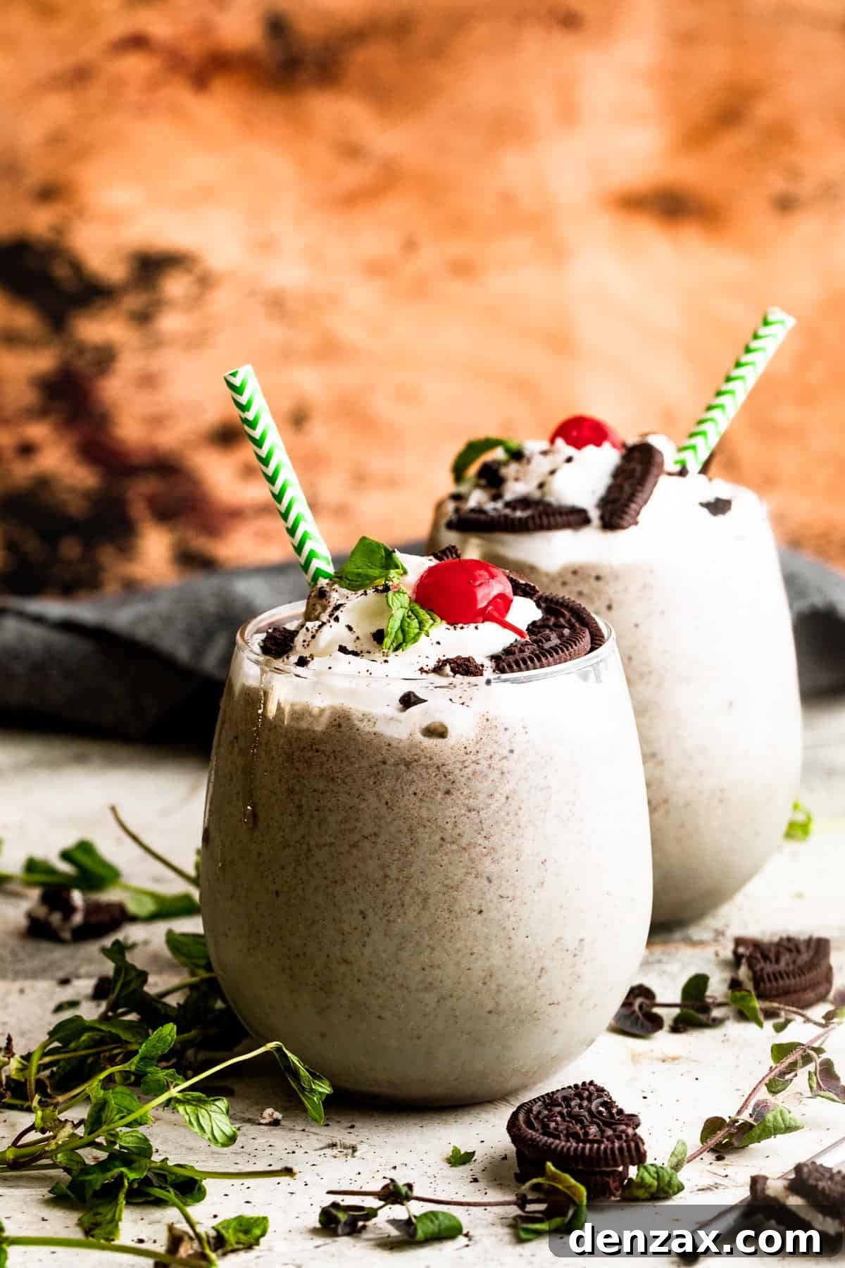 two drinking glasses filled with Shamrock Oreo McFlurry Shake, topped with whipped cream, maraschino cherries, and mint leaves.