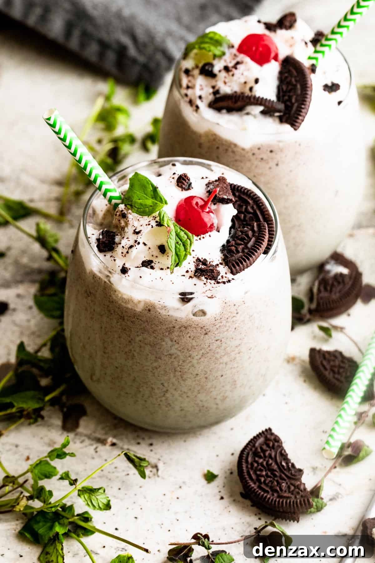 two drinking glasses filled with Shamrock Oreo McFlurry Shake, topped with whipped cream, maraschino cherries, and mint leaves.