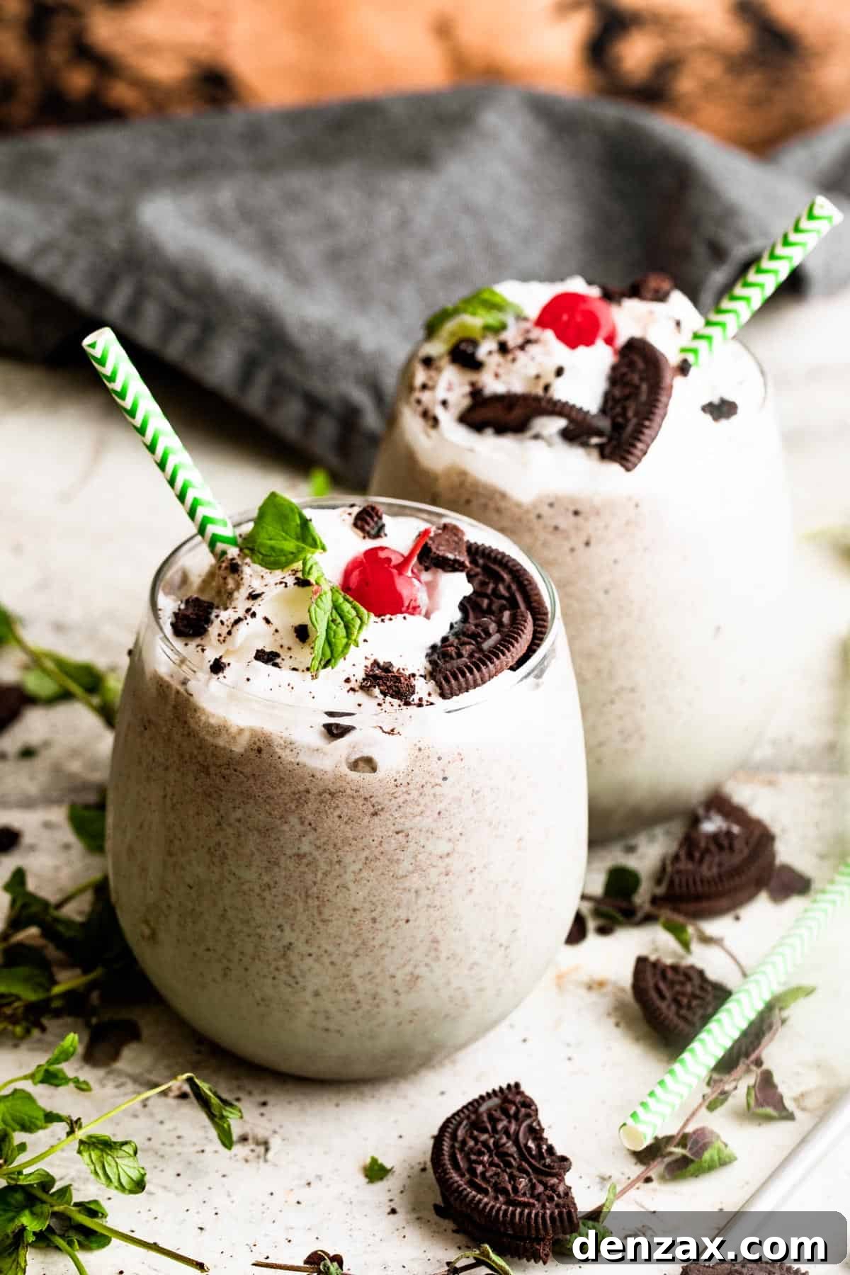 two drinking glasses filled with Shamrock Oreo McFlurry Shake, topped with whipped cream, maraschino cherries, and mint leaves.