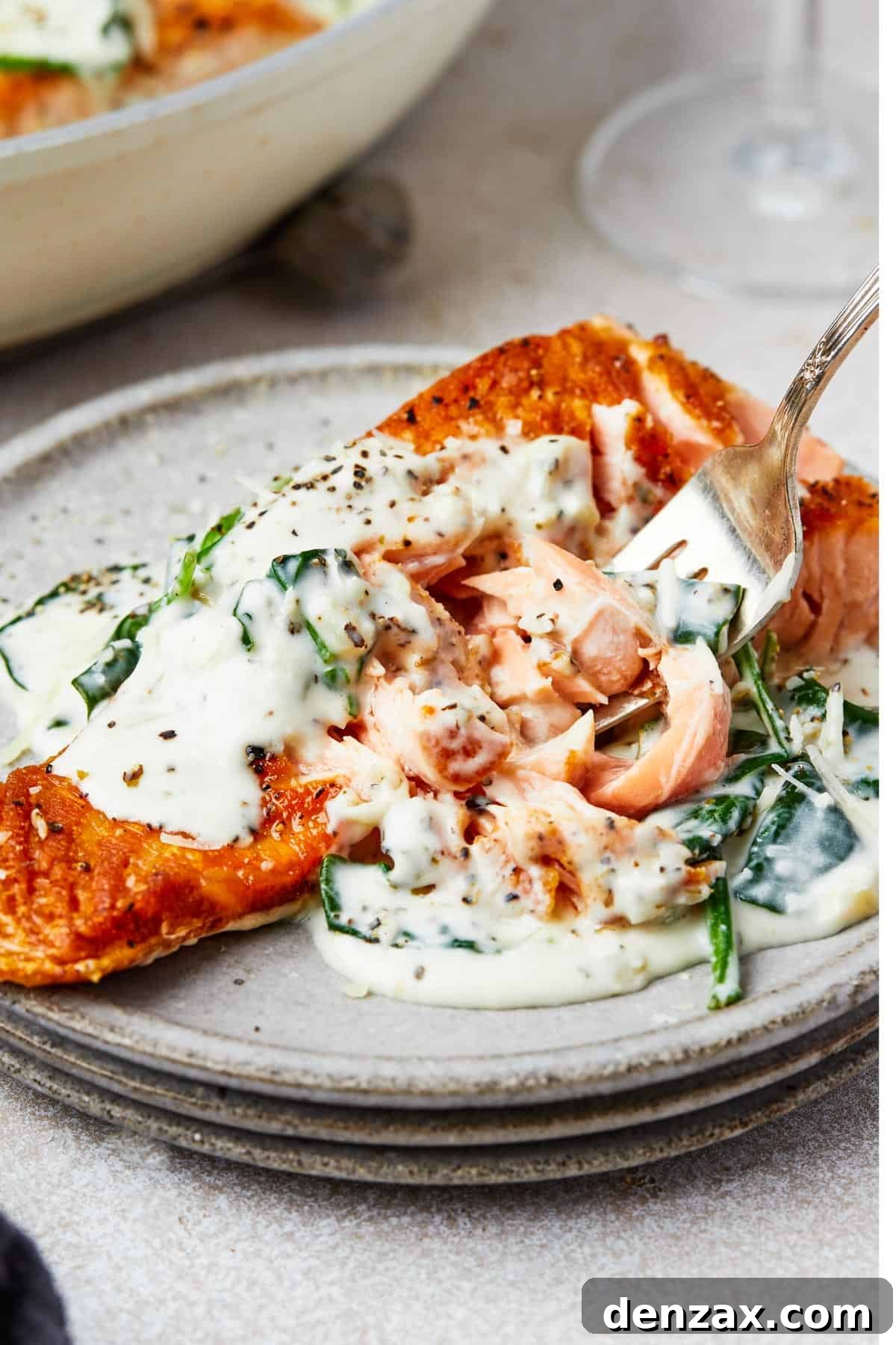 A serving of salmon florentine. A bite of the salmon is being lifted toward the camera on a fork.