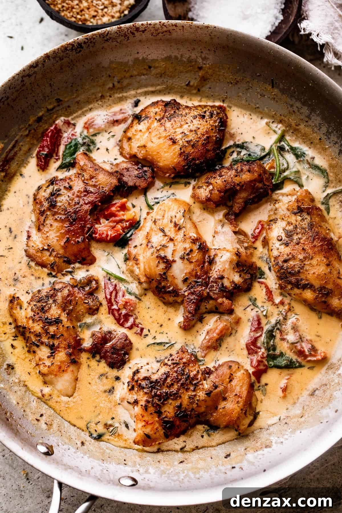 overhead shot of a stainless steel pan with boneless chicken thighs in a creamy sun dried tomato sauce.