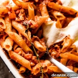 spooning out baked penne pasta from baking dish.