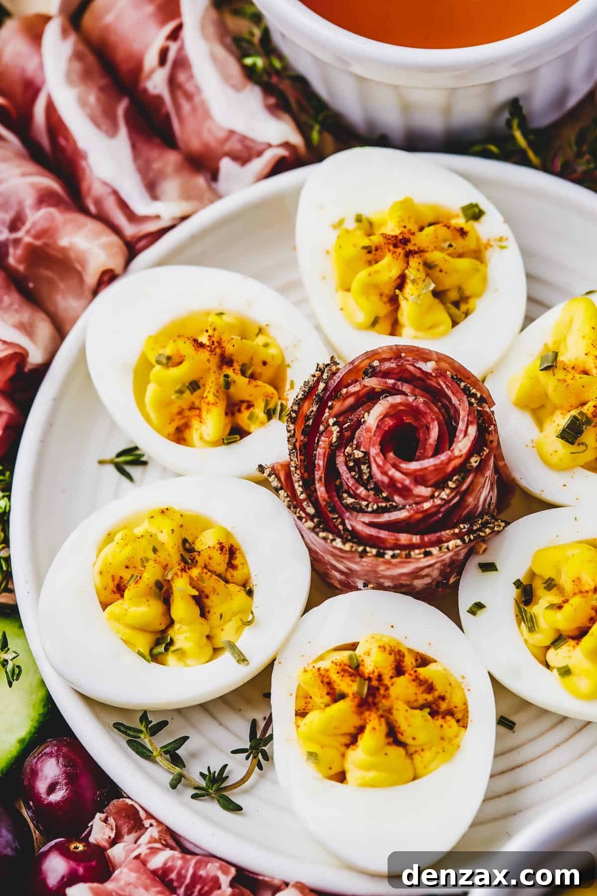 Close-up shot of a plate of deviled eggs with an artistically folded slice of coppa in the center.