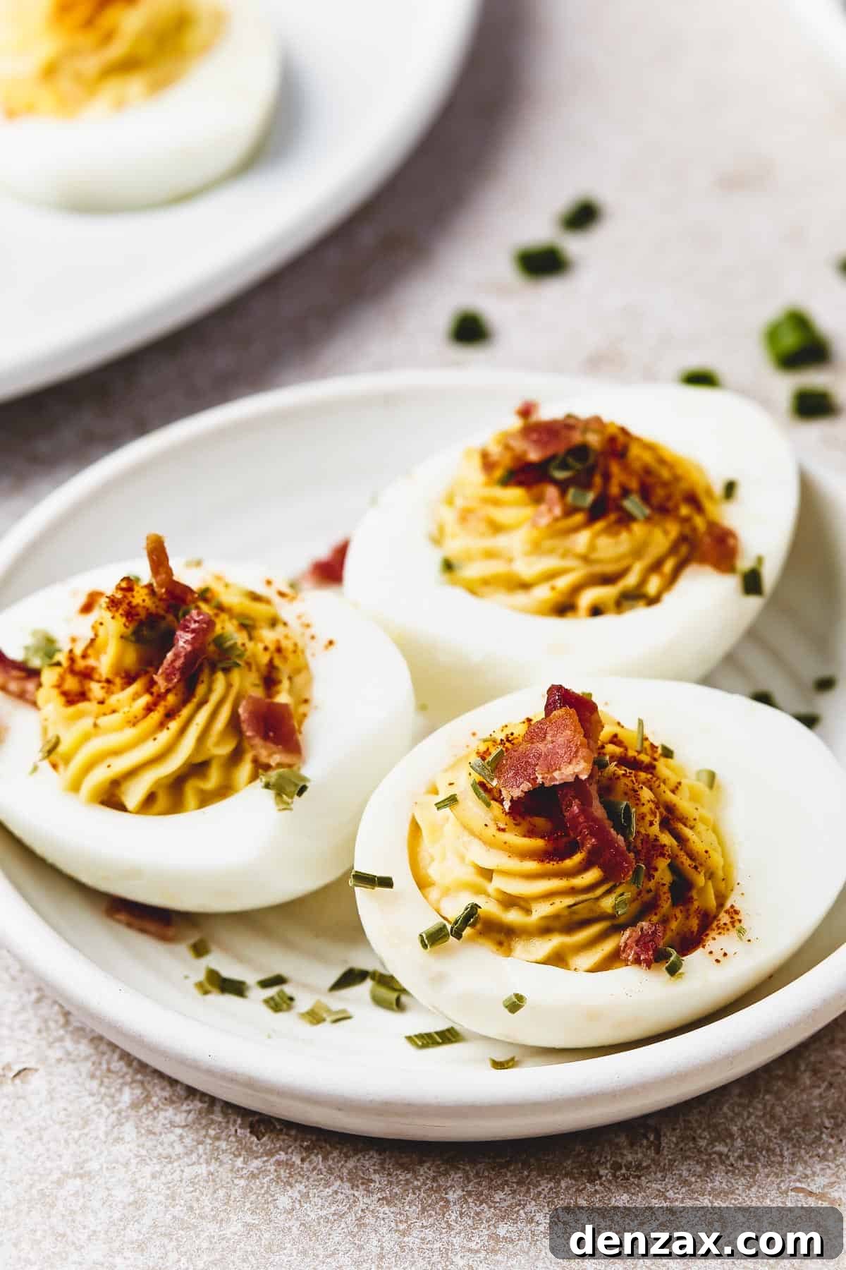 Classic Deviled Eggs Recipe: Creamy, Tangy Party Appetizer 10 A small dish with three stuffed egg halves on it, sprinkled with chives, paprika, and bacon.