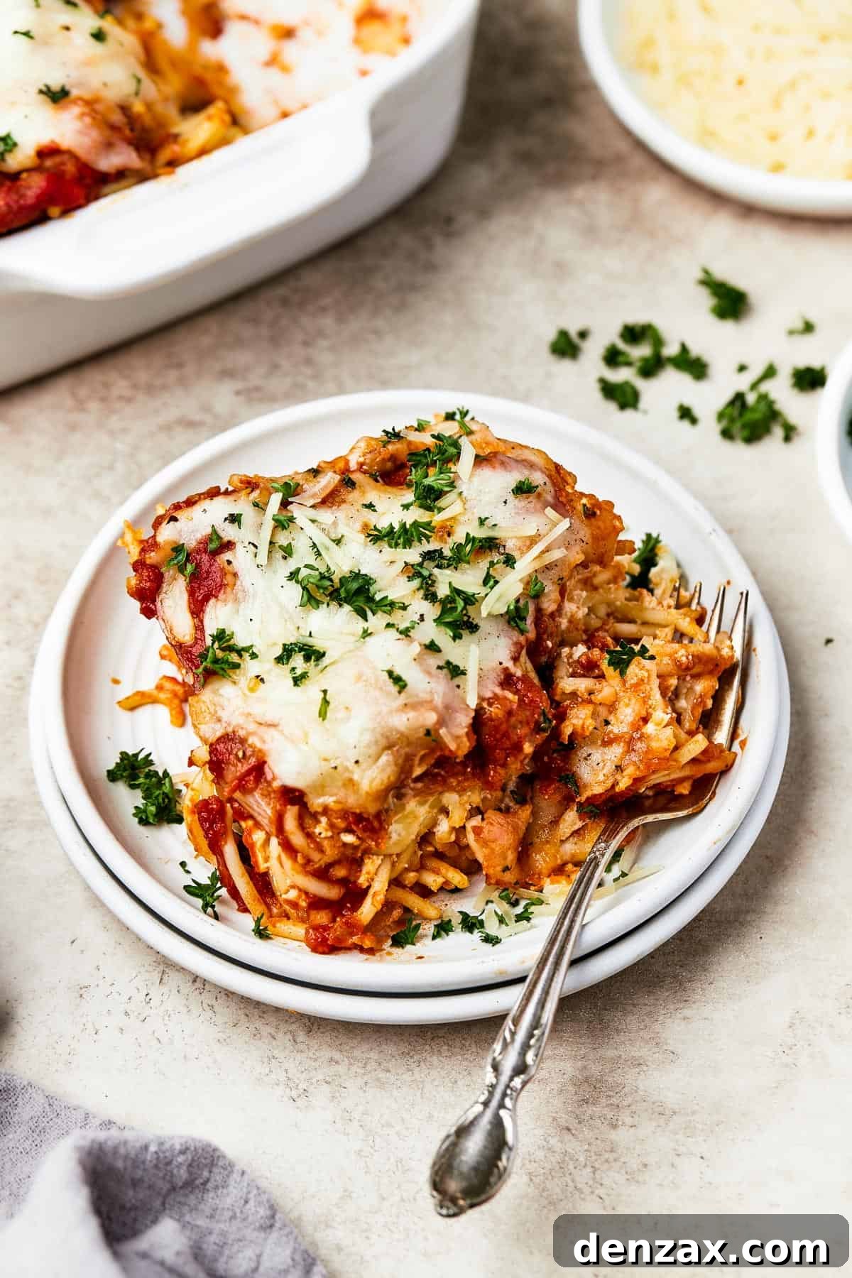 A square of baked spaghetti on a plate, garnished with parsley.