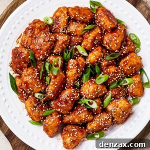 overhead shot of sweet and sour chicken served on a white plate with rice, green onions, and toasted sesame seeds.