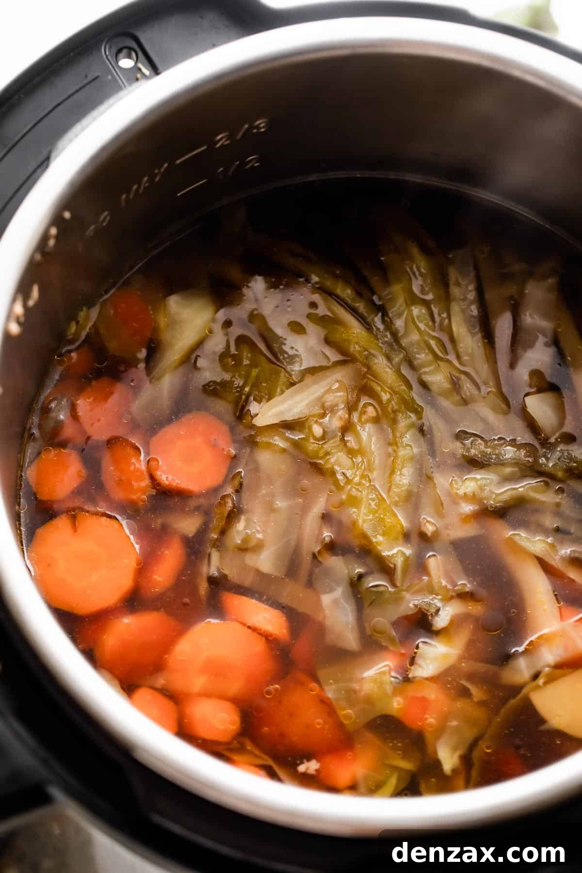 overhead shot of the insert of an instant pot filled with liquid, sliced carrots, cut potatoes, and sliced cabbage.