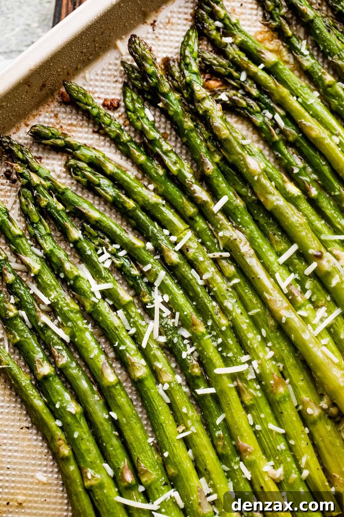 parmesan topped asparagus spears arranged on a gold-colored baking sheet.