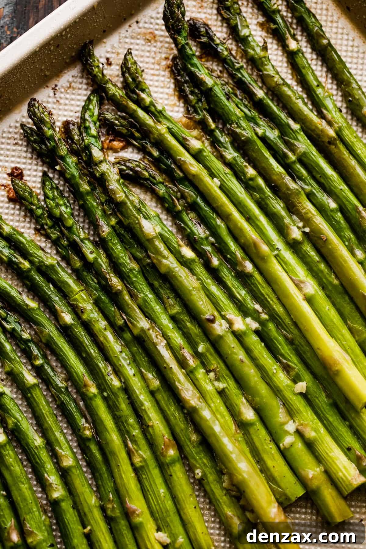 close up shot of asparagus spears arranged on a gold-colored baking sheet.