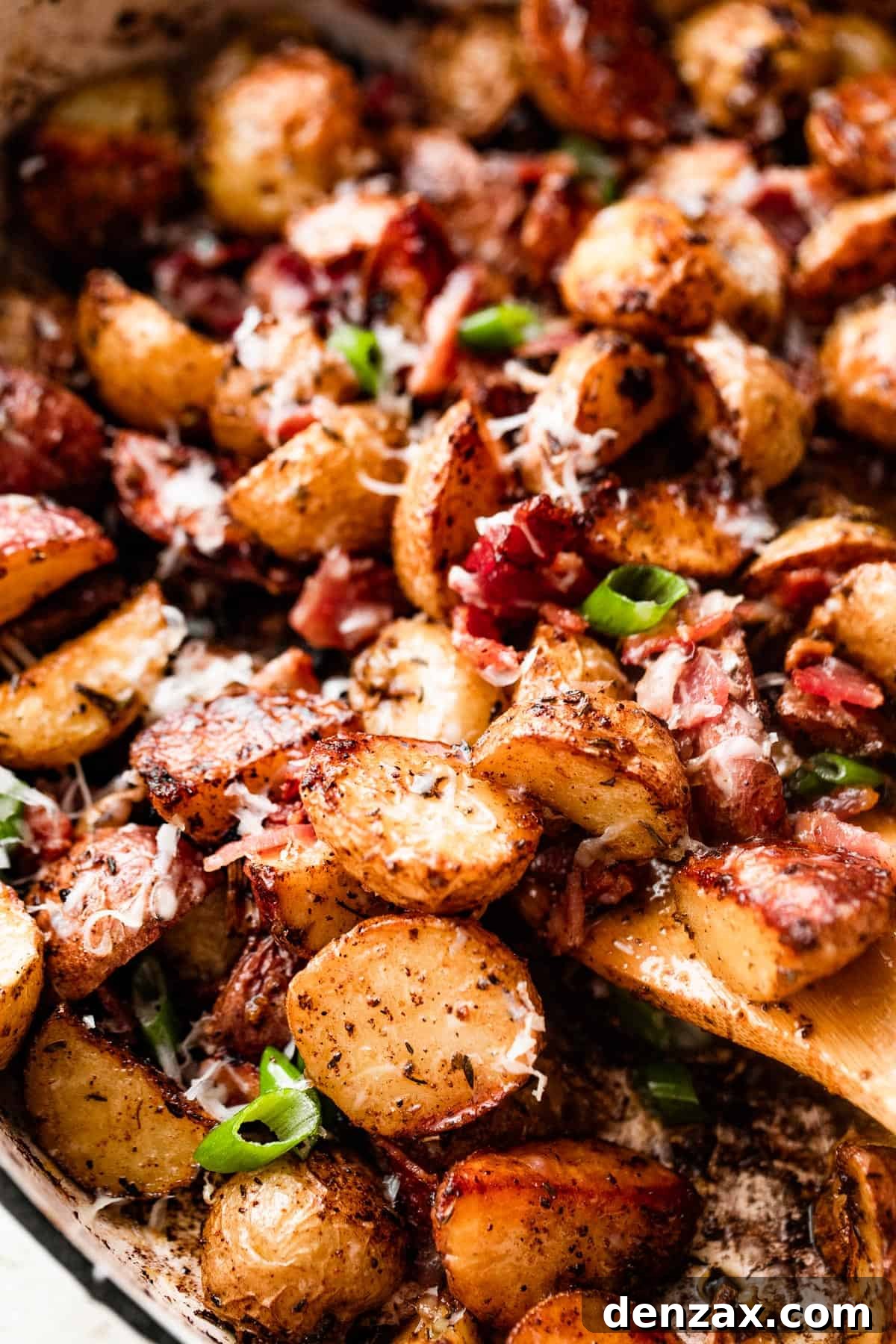Crispy Roasted Potatoes with Bacon, Cheese, and Herbs 6 close up shot of a wooden spoon stirring through roasted potatoes with bacon and cheese.