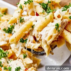 close up shot of chicken alfredo pasta being scooped out of a casserole dish.