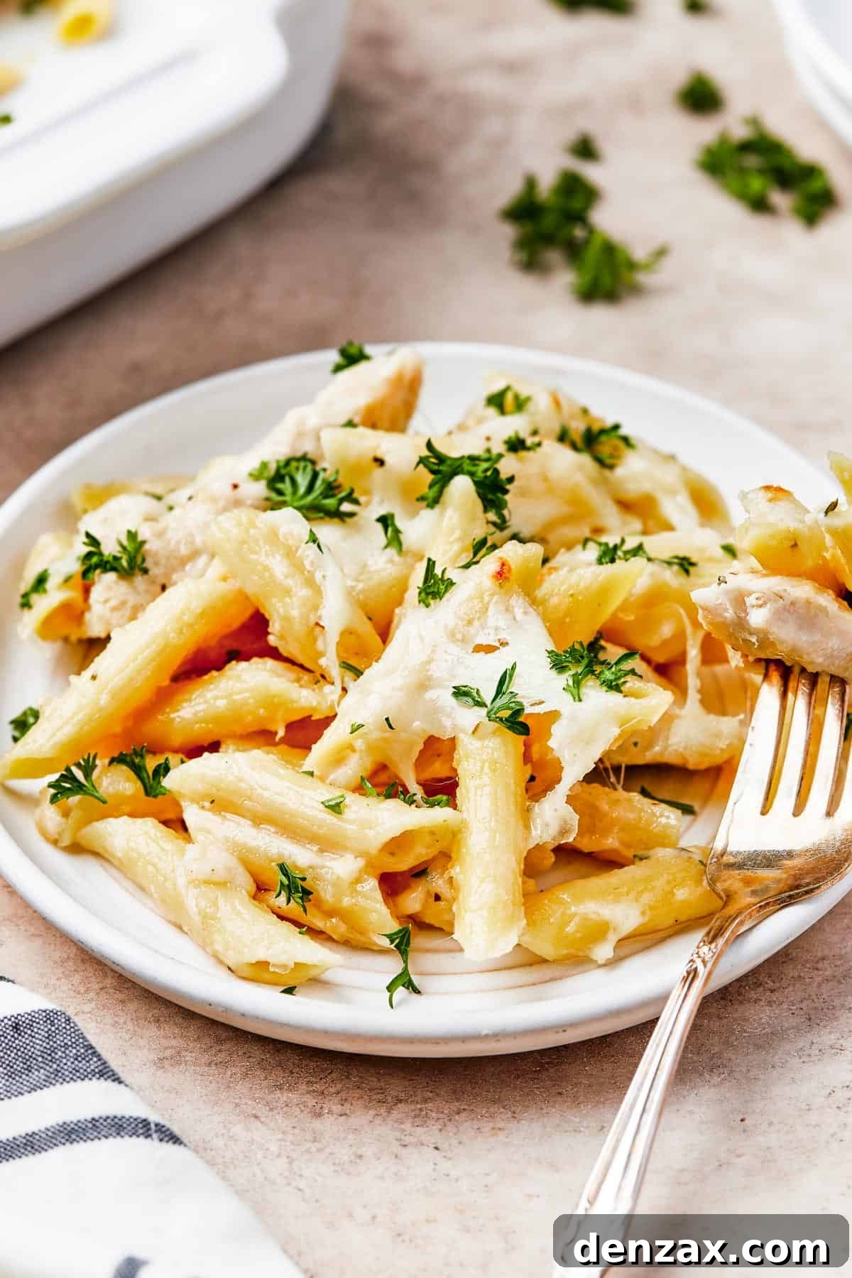 Chicken pasta with creamy sauce and melted cheese, on a small serving plate with a fork.